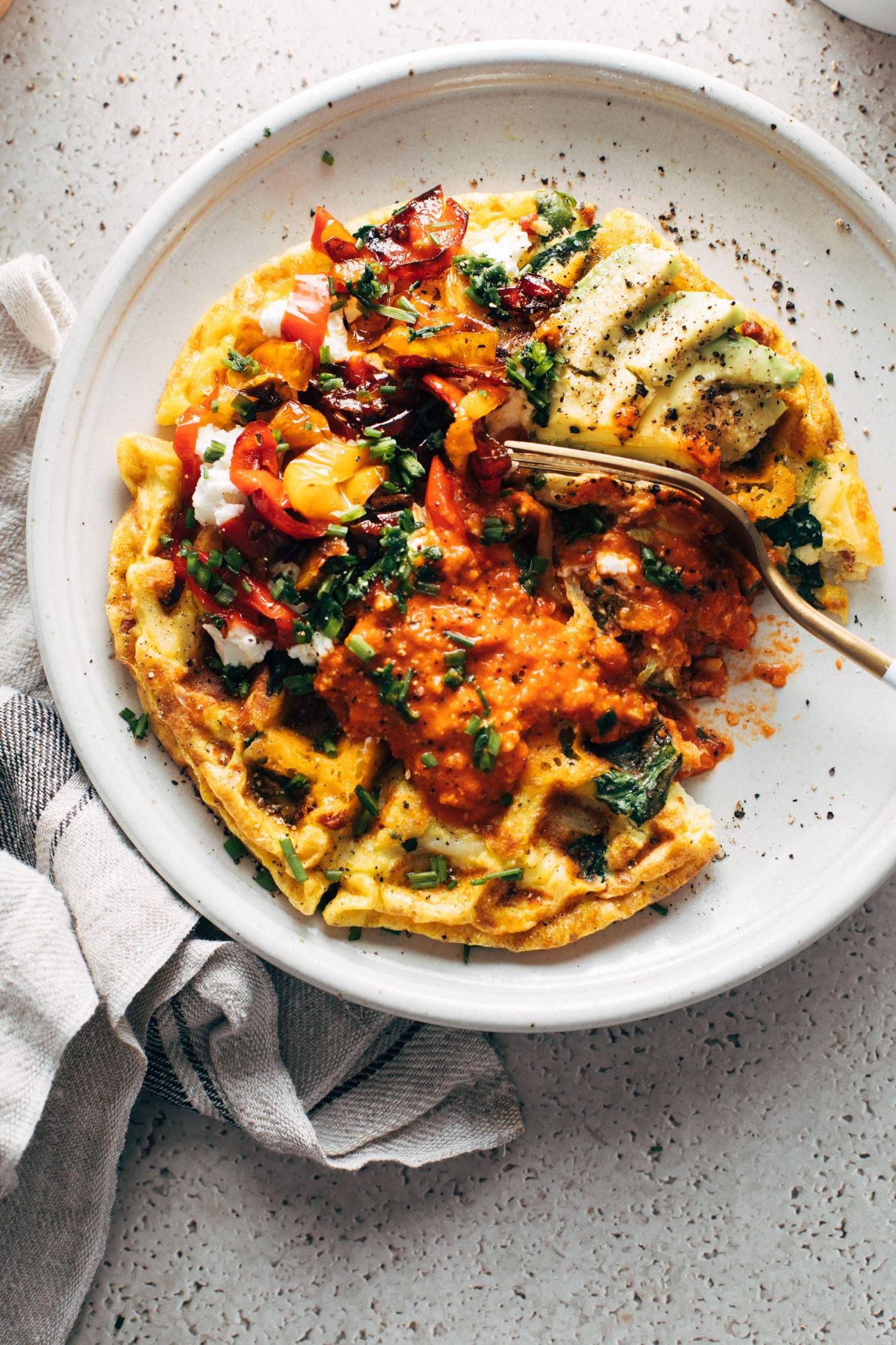 Egg waffle on a plate loaded with toppings and a fork