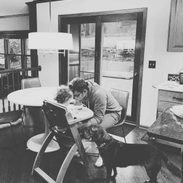 A man sitting on a chair facing a baby who is having food.