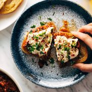 White hand grabbing Zaalouk toast on a plate