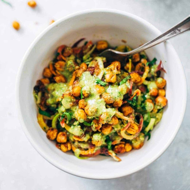 Spiralized veggies in a bowl with chickpeas and green sauce.